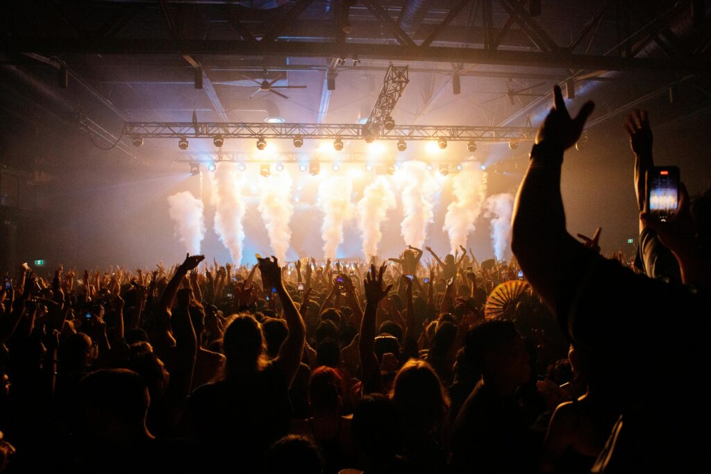 Energetic crowd enjoying a concert with dynamic lighting and smoke effects in an indoor venue.
